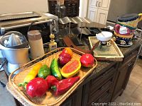 Wide view of kitchen countertop with collection of appliances and kitchen accessories including juicer, coffee grinder, spice rack, wine bottle holders, bamboo tray with artificial fruit, cookie jar set
