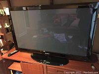 Samsung PN50B450 plasma television on wooden stand, screen off, shows black glossy frame and circular base.