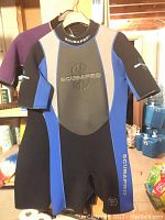 Scubapro shorty wetsuit on hanger showing front mainly black with blue panels and Scubapro branding.