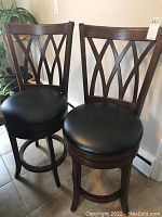 Front view of two dark brown wooden swivel bar stools with lattice back and black padded seats