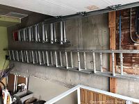 Two aluminum ladders laid on a concrete floor, shorter ladder approximately 90 inches, longer ladder is full extension.