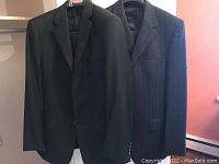 Two men's suits hanging, dark color with classic lapels, showing outer front.