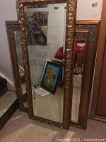 Two mirrors leaning against wall, full view of both frames and reflective surfaces