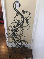 Front angled view of decorative metal wine rack showing rows of circular holders for 12 wine bottles and leaf motif.