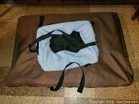 Medium dog tent-shaped carrying case in brown fabric on floor with brown dog bed and small dog carrier bag with blue fleece lining on top.