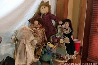 Five vintage dolls including Santa with reindeer, wooden angel, Pet Zone cat doll, and two dress-wearing dolls on a shelf