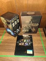 Boxed set of Star Wars Original Trilogy VHS tapes and The Force Awakens DVD on wooden surface against wood background.
