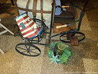Wide view showing the metal and wood tricycle plant stand, lighthouse birdhouse, and faux succulent candle planter placed on floor