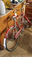 Full rear side view of vintage Triumph bicycle showing red frame, rear fender with reflector, and wide curved chrome-style handlebars with white grips.