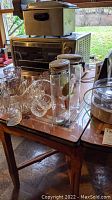 Table covered partially with various kitchen and glass items, shows the tabletop and some wear.
