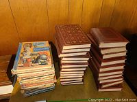 Photo showing three different stacks of vintage books including a large set of brown hardcover books, a colorful set of illustrated books, and a smaller set with colorful spines of encyclopedia volumes.
