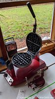 Open red Waring Pro waffle maker showing round waffle plates with deep grid pattern and lever handle.