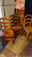 Photo showing three wood chairs: two matching ladder-back chairs with carved details, and one additional wooden chair. Chairs show wear and stains.
