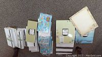 Photo showing stacks of white and green business envelopes, decorative stationery sheets with floral borders, and a few birthday greeting cards.