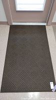 Full view of brown entrance rug placed in front of door, showing rectangular shape and textured geometric pattern.