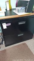 Front view of black 2-drawer file cabinet with wood grain top and two drawer handles.