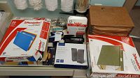 Photo showing several packs of Pendaflex hanging folders in blue and green, a pair of boxed powered multimedia speakers, and various small office supplies on a desk.