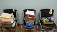 Three chairs holding various office supplies: folders, binders, papers, and boxes