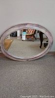 Full frontal view of oval beveled glass mirror with purple distressed frame, showing carpet floor and wall background.