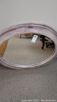 Front view of oval beveled mirror showing entire purple frame and glass surface, placed on carpeted floor.