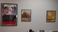 Wide shot of three framed advertising posters mounted on a wall with slight reflections and visible wear.