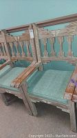 Photo showing two Aztec style wooden arm chairs with green cushioned seats, carved backs and arms, distressed wood finish.
