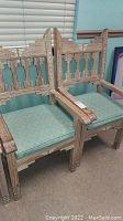 Two wooden arm chairs with Aztec-inspired geometric backrests, distressed finish, and green upholstered seat cushions.