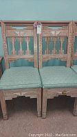 Four wooden chairs with Aztec cutout design and green cushions in a row.