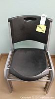 Front view of a single metal frame chair with black plastic seat and backrest, showing some dust and need for cleaning.