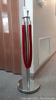Front angle view of stainless steel guidepost with attached red velvet rope, showing round base and post height.