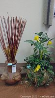 Two planters/vases with faux plants: a green pot with yellow flowers and ivy, and a brown textured vase with tall reeds.