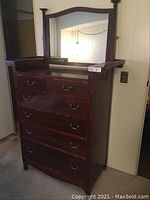 Full view of antique wooden bureau with attached hinged mirror, showing four large drawers with brass handles and wooden posts supporting the mirror.
