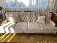 Full front view of three-seat tufted sofa showing beige patterned upholstery, carved wood frame and two throw pillows.