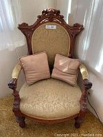 Full view of antique armchair with two beige throw cushions on seat.
