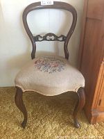 Front view of antique wooden slipper chair showing curved backrest, carved decorative detail, and floral needlepoint fabric seat.