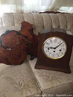 Both clocks are shown side by side on a patterned sofa, displaying the overall size and wood finishes.