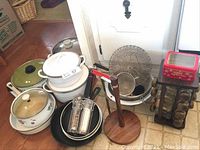 Photo showing assorted ceramic pots with lids, two cast iron frying pans, metal kitchen sieves, wooden paper towel holder and spice rack with glass jars.