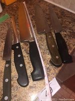 Four knives arranged on a countertop with measuring tape beside them showing blade length variation.