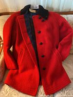 Jacket laid flat showing front exterior with button closure, welt pockets, and knit collar.