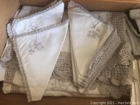 White or cream napkins with floral embroidery and crocheted edges arranged in a box