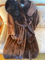 Full shot of brown mink fur coat, brown gloves, and black fur neck wrap displayed on sofa