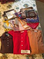 Lot overview showing three sweaters in brown, red, and peach with a pile of colorful scarves behind them.