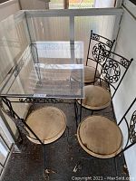 Set of rectangular fiberglass top table with wrought iron frame and four matching wrought iron chairs with attached vinyl seat cushions. Visible dirt and wear on cushions and frame.
