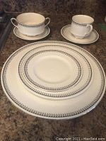 Stack of dinner, lunch and dessert plates with a double-handled bowl and tea cup on counter