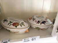 Two covered vegetable dishes, oval and round, with fruit and gold trim designs on shelf