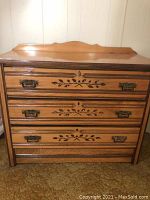 Front view of solid wood sideboard showing three drawers with decorative leaf pattern and metal handles.