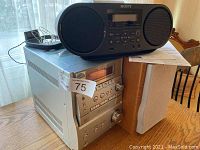Two Sony CD players shown together: black portable player on top of silver stereo system with attached speaker on wood table.