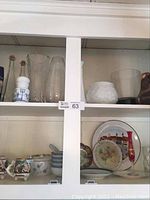 Wide view of cabinet shelf showing glass vases, milk glass pieces, Chinese bowls with spoons, and vintage china plates.