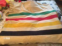 Full view of cream colored wool blanket with green, red, yellow, and navy stripes