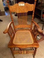 Front view of wooden chair showing carved top backrest and armrests with woven wicker seat insert.